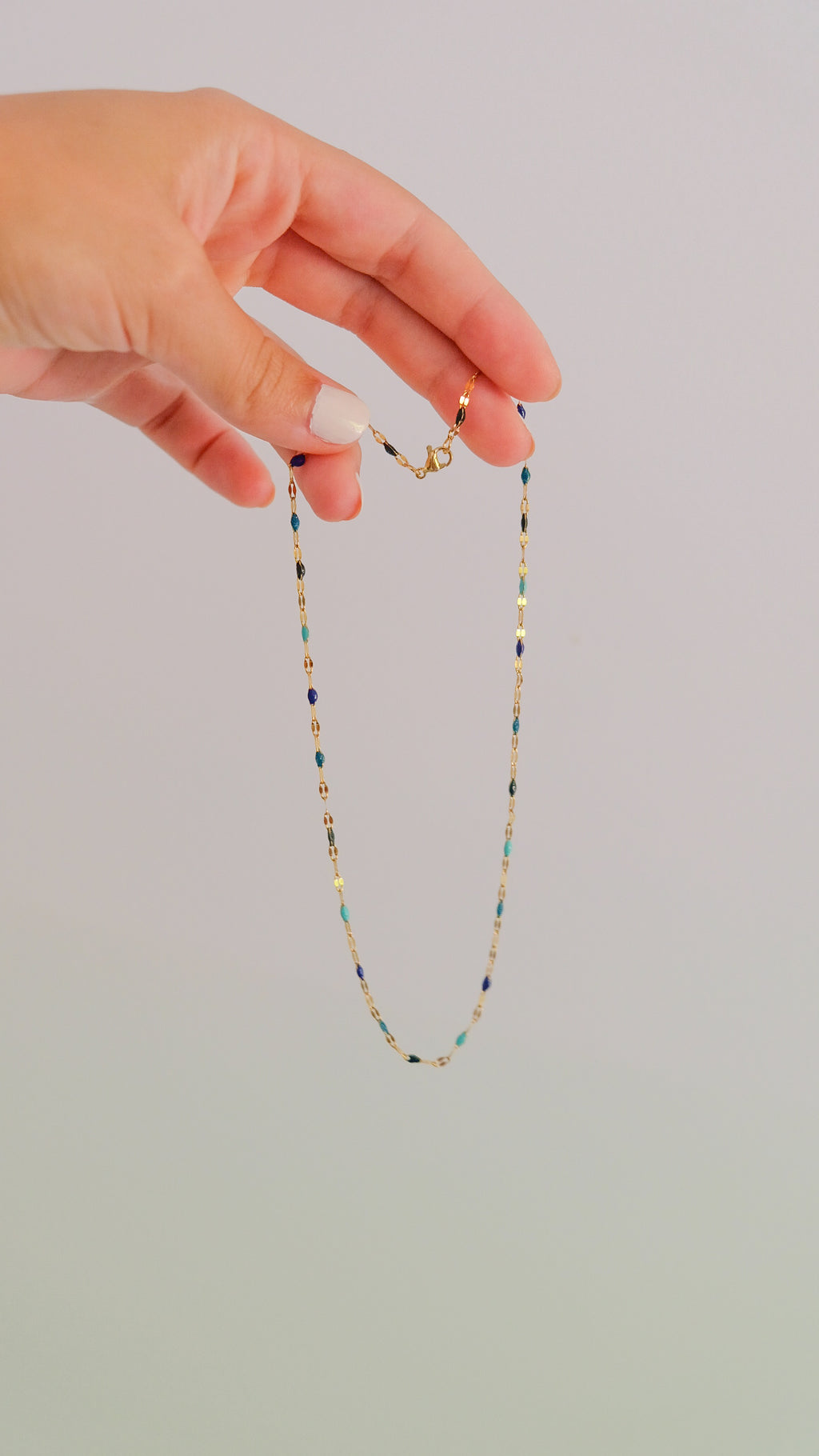 Hand holding a delicate beaded necklace against a plain background