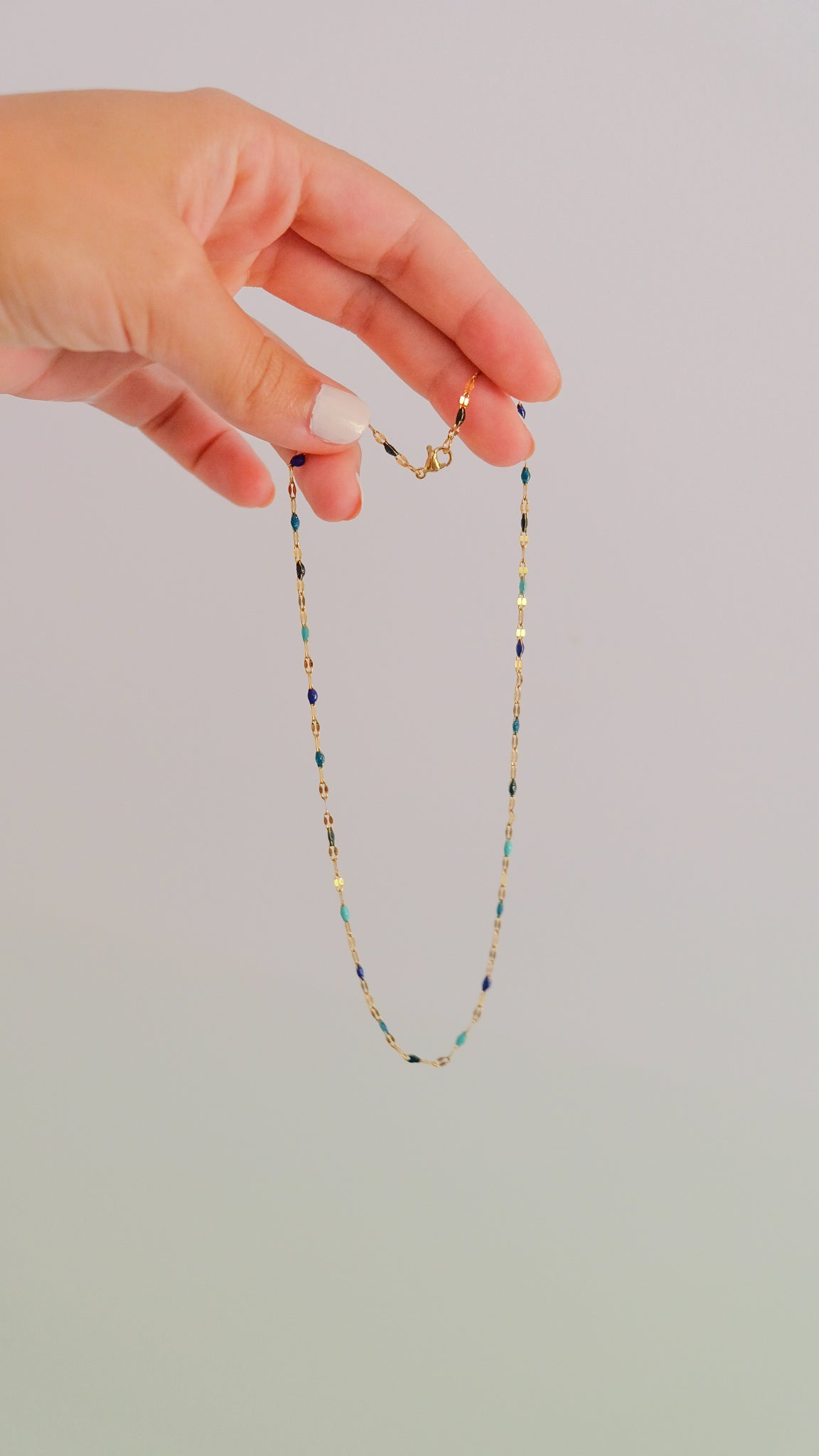 Hand holding a delicate beaded necklace against a plain background