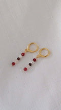 Gold earrings with red beads on a light gray background