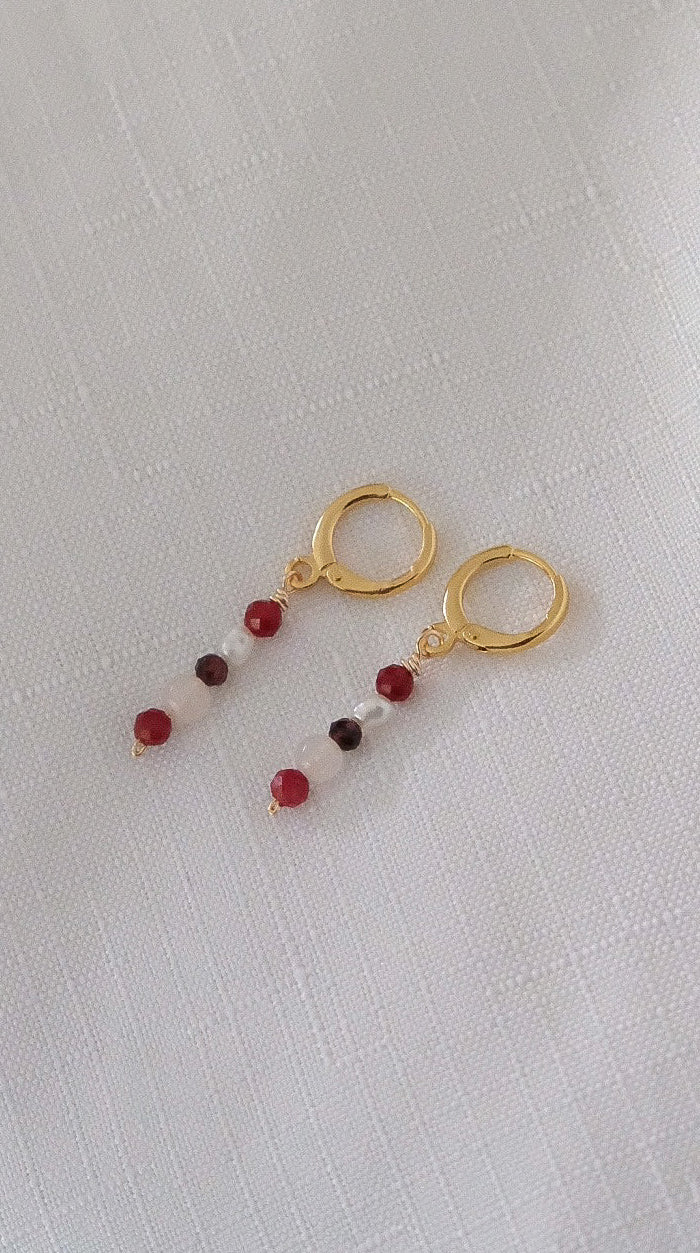 Gold earrings with red beads on a light gray background