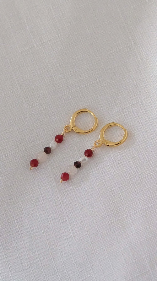 Gold earrings with red beads on a light gray background