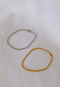Two gold and silver chain bracelets on a white fabric background