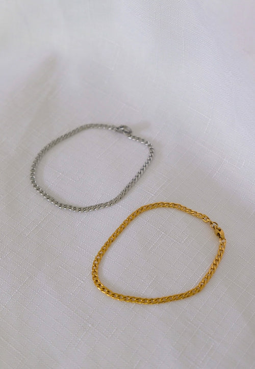 Two gold and silver chain bracelets on a white fabric background