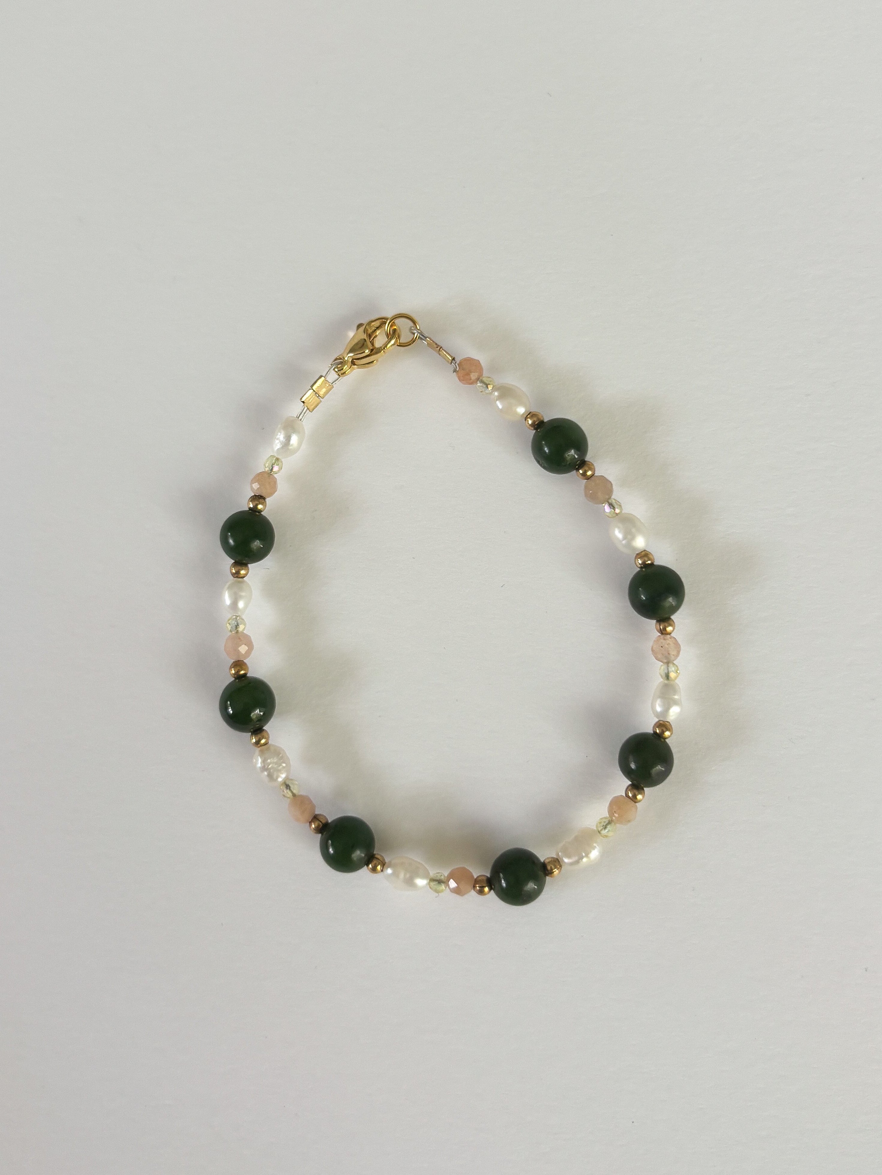Bracelet with green beads and gold accents on a light gray background