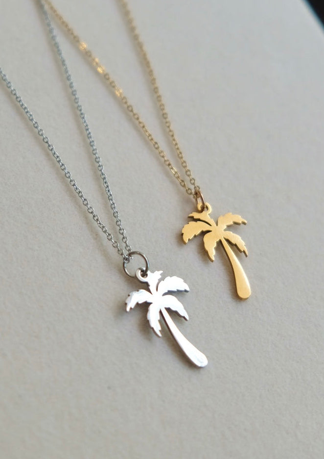 Two necklace pendants shaped like palm trees on a light gray surface.